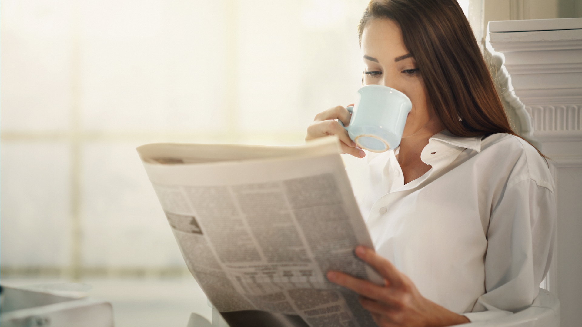 woman sipping coffee and reading the newspaper